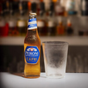 bottiglia di Peroni Nastro Azzurro Capri con bicchiere vuoto accanto
